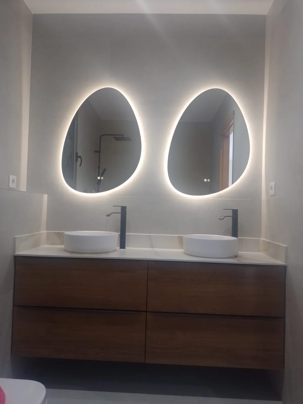 Mueble de baño suspendido de madera con dos lavabos de sobre y dos espejos ovalados con luz LED