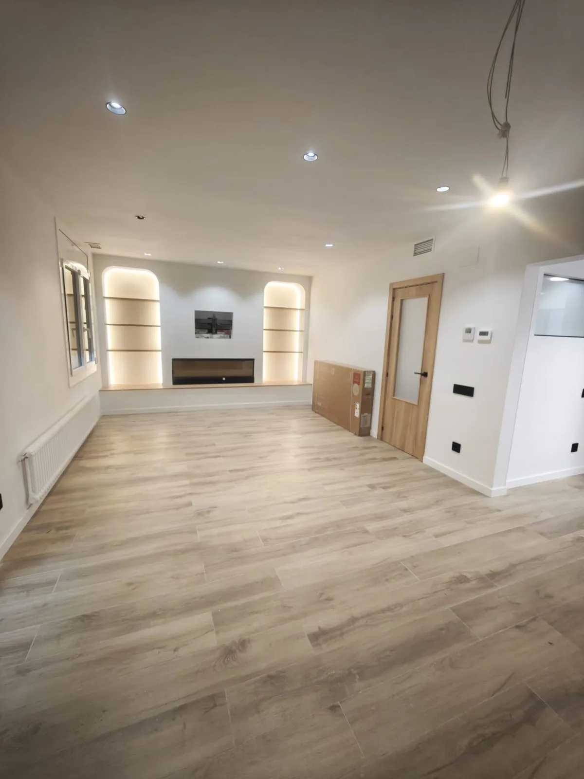 Salón reformado con suelo laminado, hornacinas con luz indirecta, puerta de madera y focos en el techo