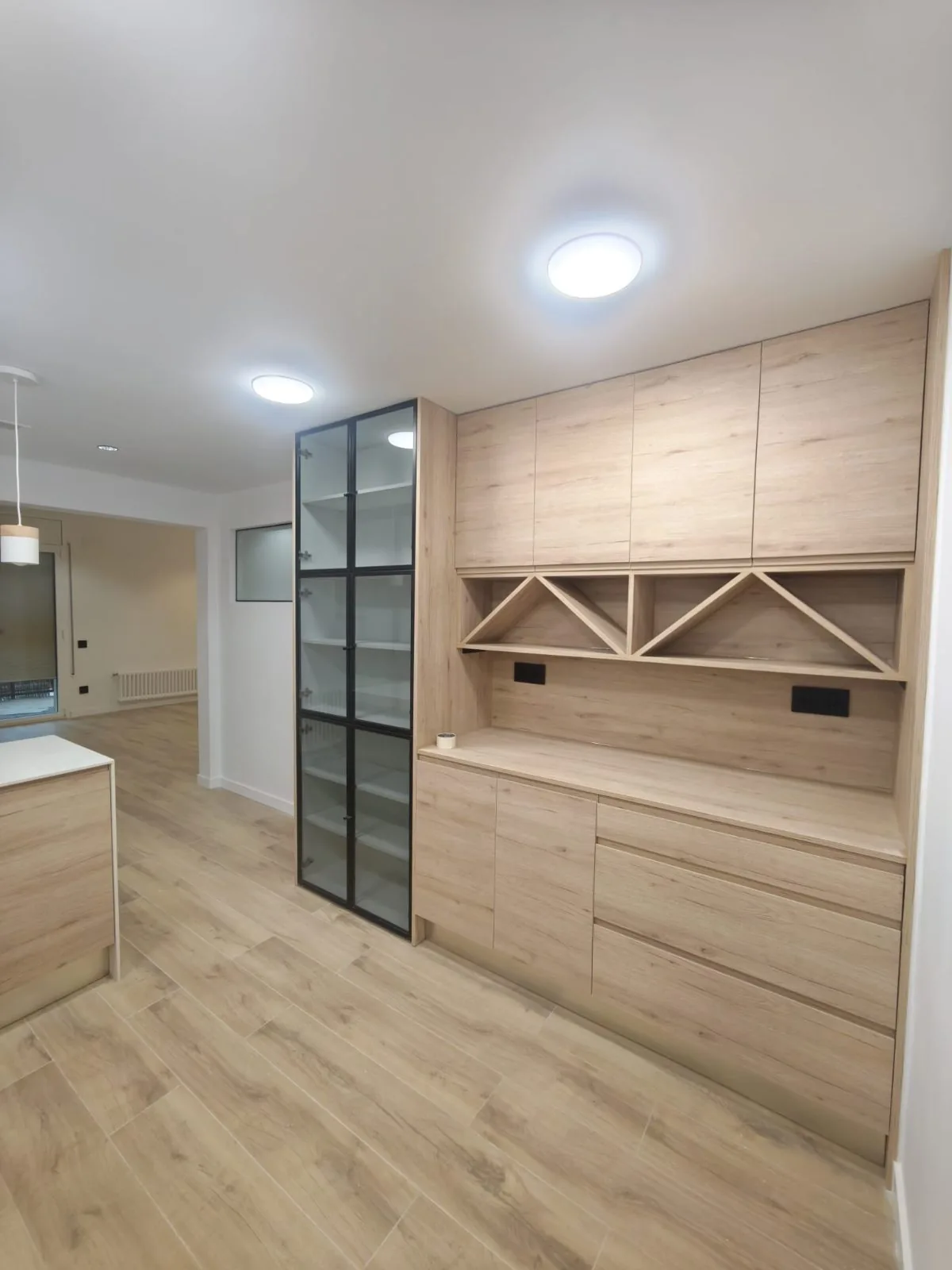 Mueble a medida de madera clara con vinoteca en forma de rombos y vitrina con puertas de cristal y marco negro