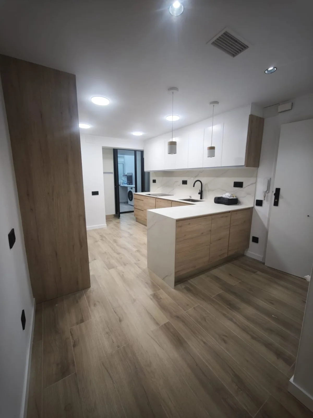 Cocina abierta con península, muebles de madera y blancos, suelo de parquet y lámparas colgantes