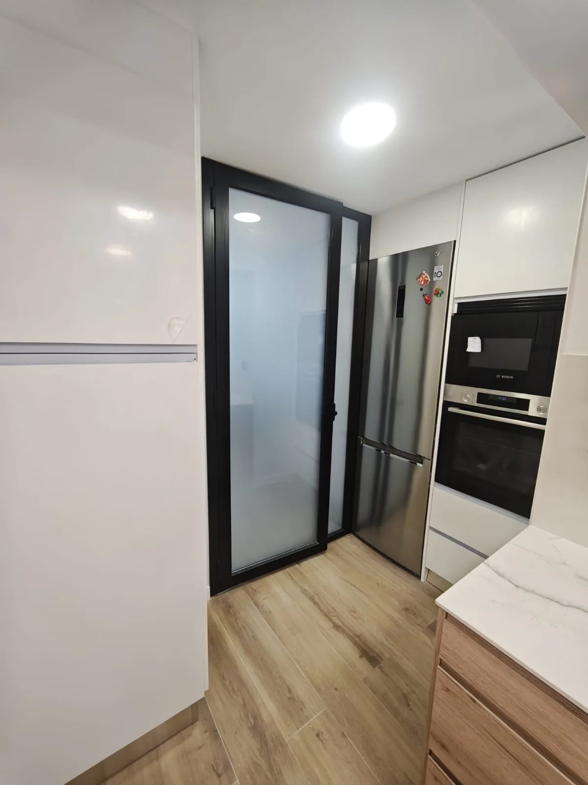 Cocina con frigorífico, horno y microondas integrados, encimera de mármol y puerta de cristal esmerilado
