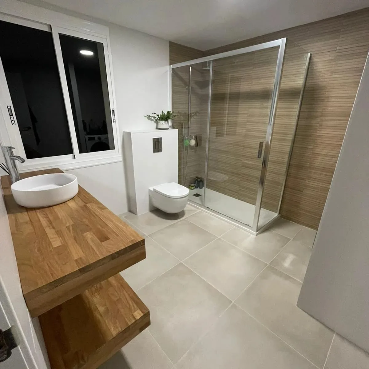 Baño con mampara de ducha, encimera de madera maciza con lavabo de sobre, inodoro suspendido y ventana