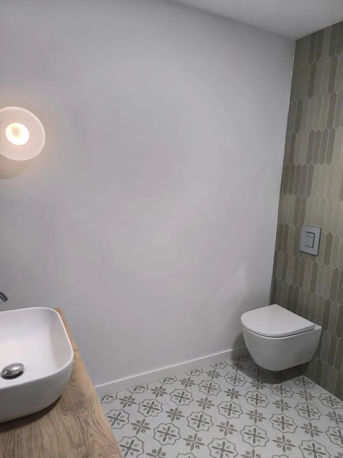 Aseo con inodoro suspendido, suelo hidráulico, revestimiento vertical verde y lavabo sobre encimera de madera